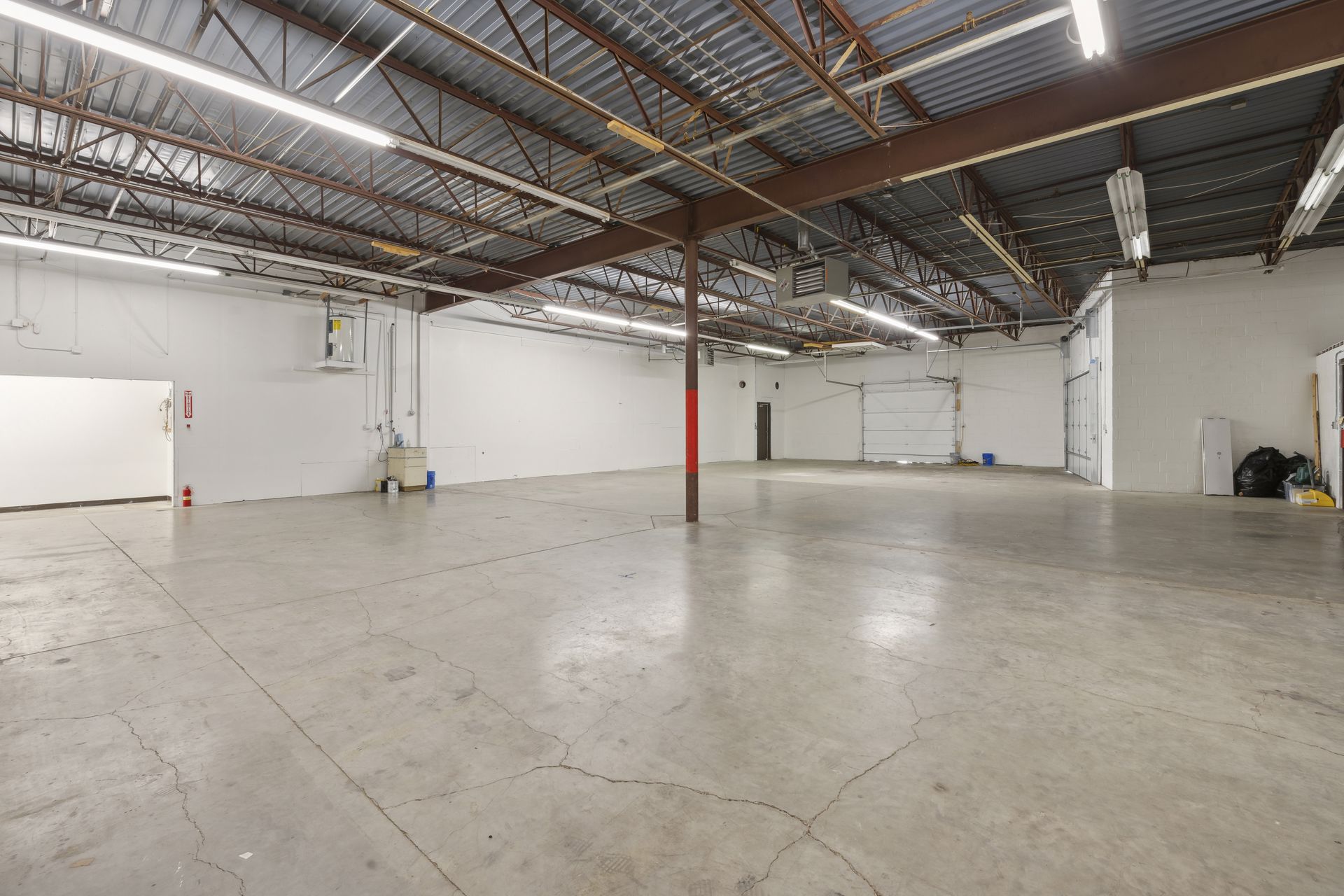 Warehouse bay with a concrete floor and strip lighting looking toward an overhead door