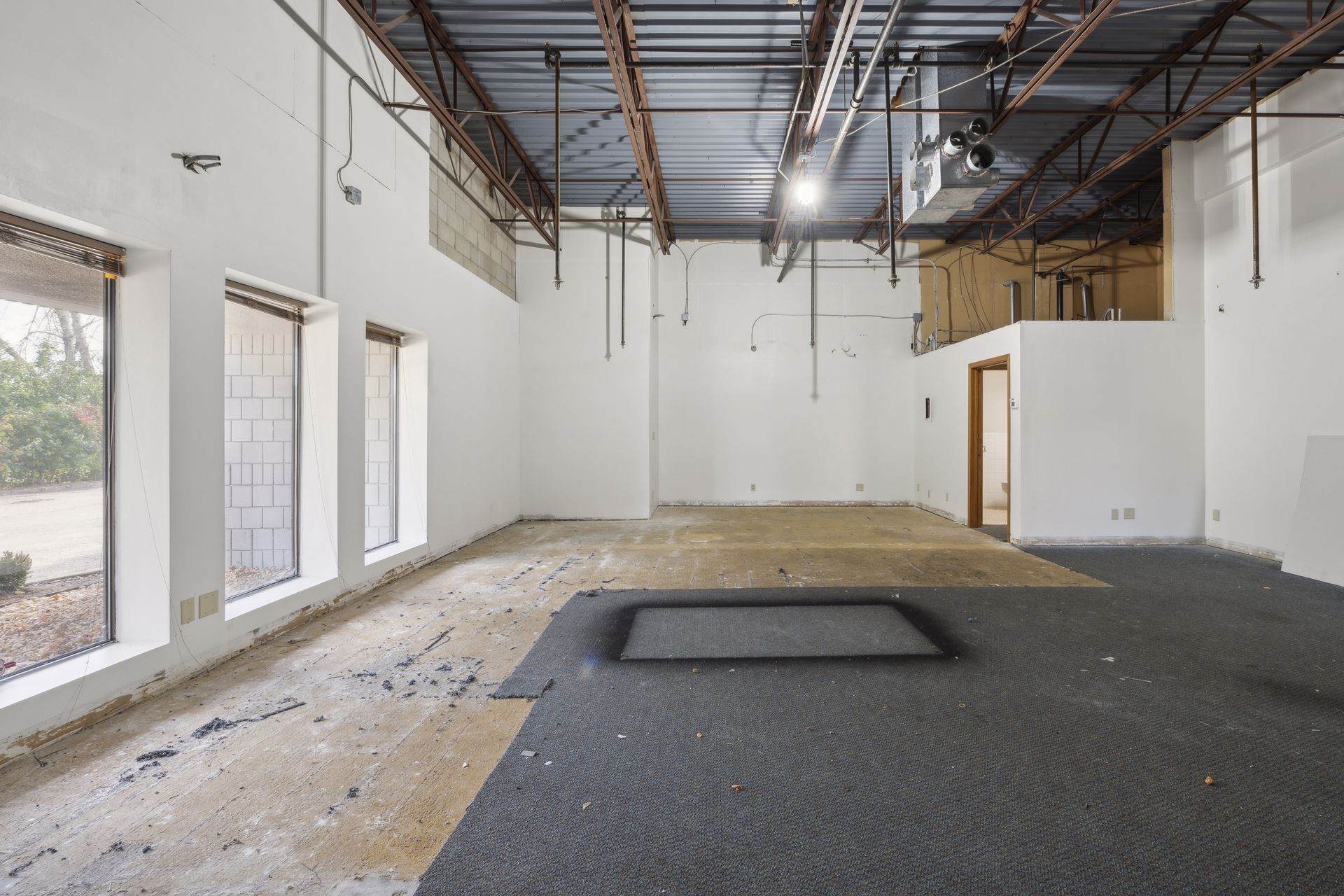 Interior space under renovation with exposed roof structure, bare walls and a partly stripped floor