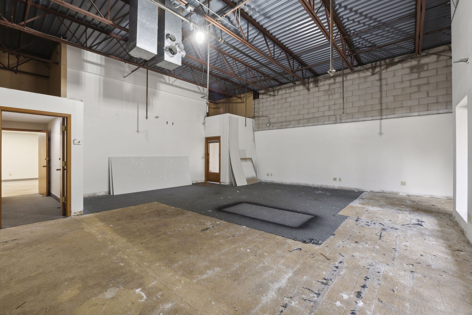 Interior space under renovation with drywall sheets leaning against the wall and a doorway to a carpeted area