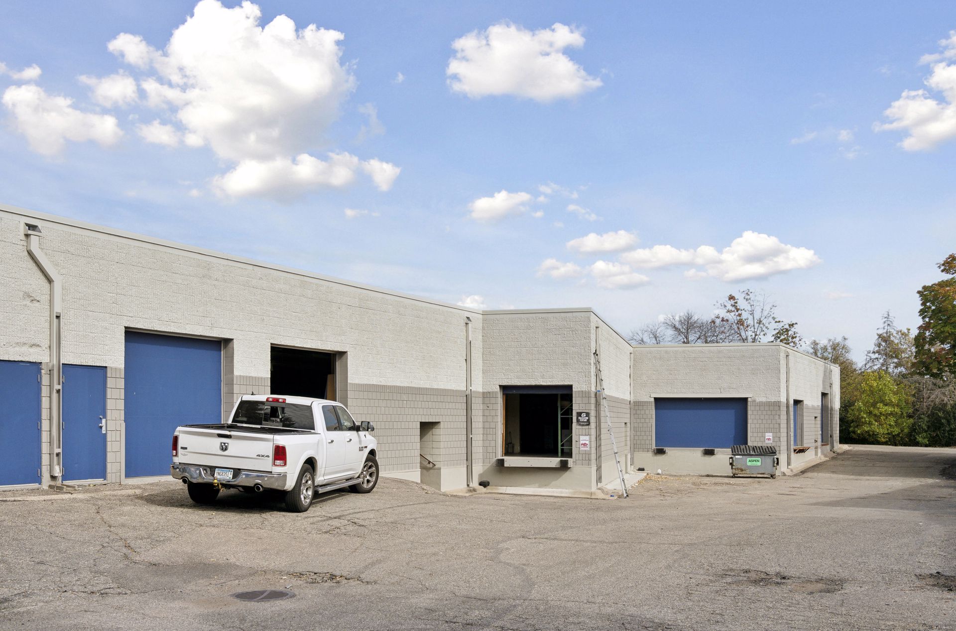 Rear drive lane with blue overhead loading doors, one open, and a pickup truck parked alongside