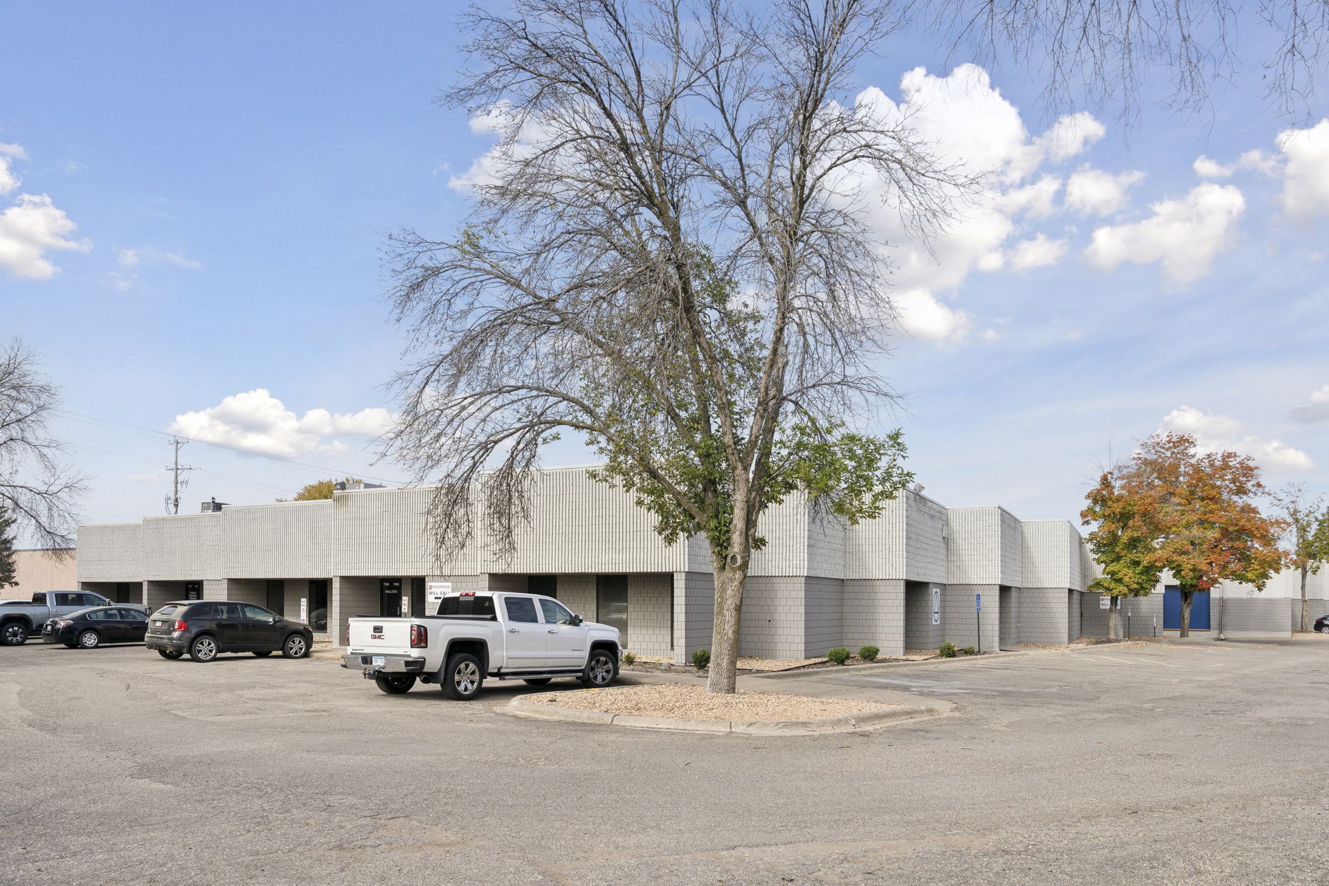 Light grey block commercial building seen across a surface parking lot with vehicles parked in front