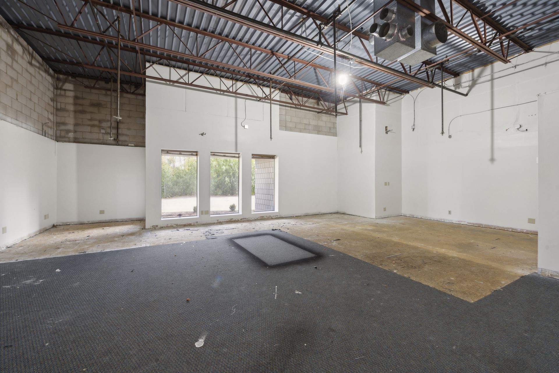 Interior space under renovation with a glazed storefront entrance and exposed overhead structure