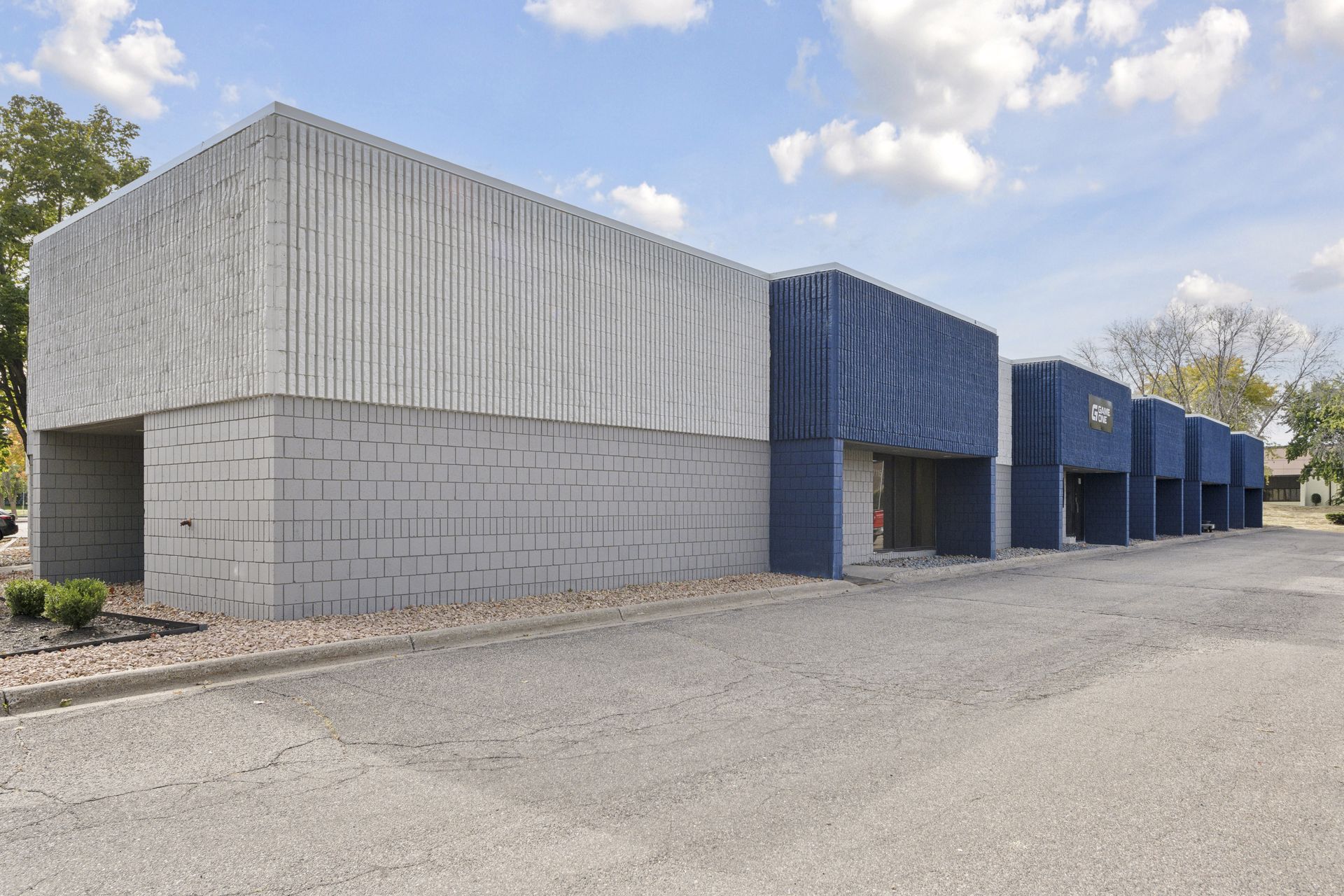 Single-storey concrete block building with a row of blue projecting entry bays along a paved drive