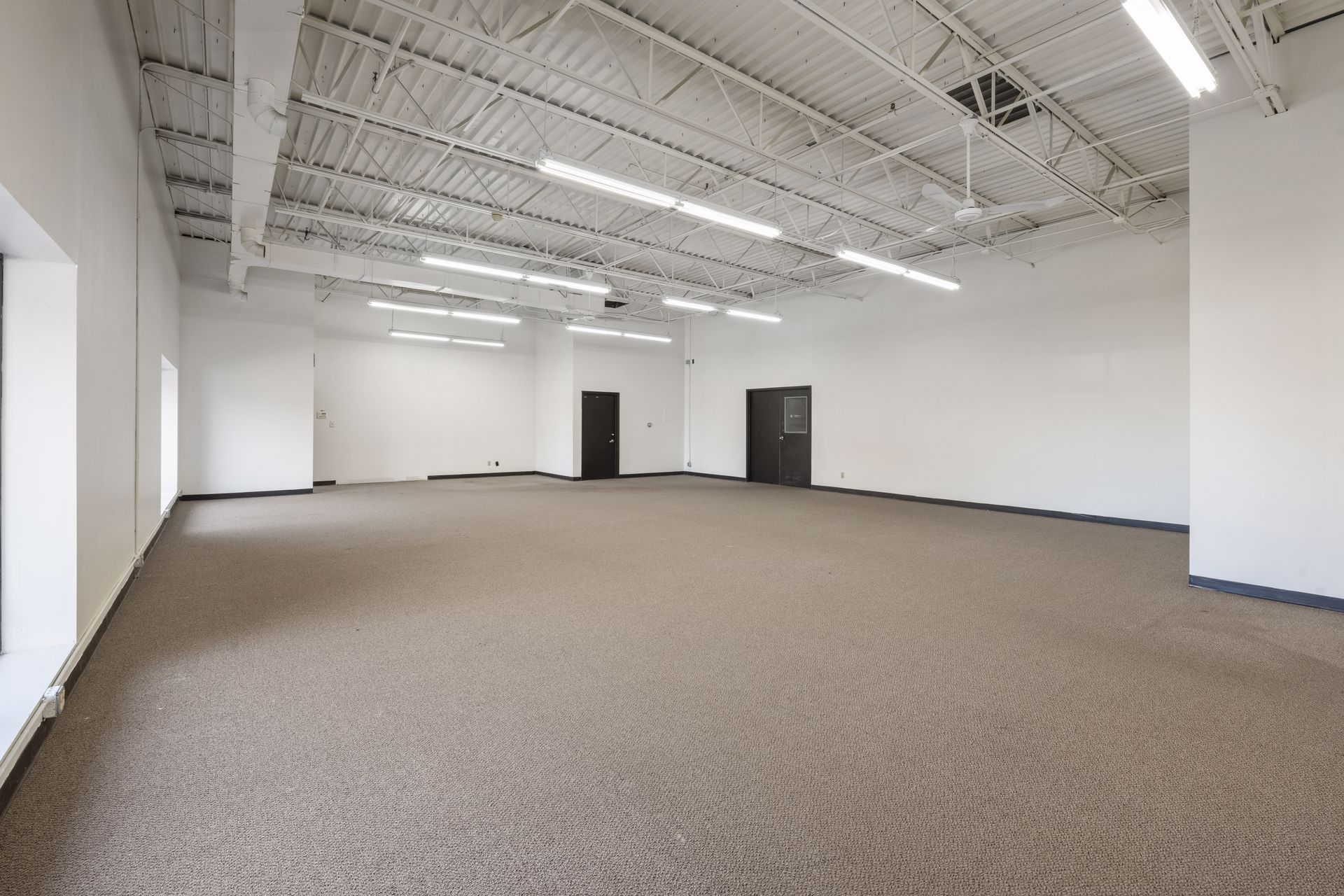Large open carpeted suite with exposed overhead ductwork and two doors on the far wall