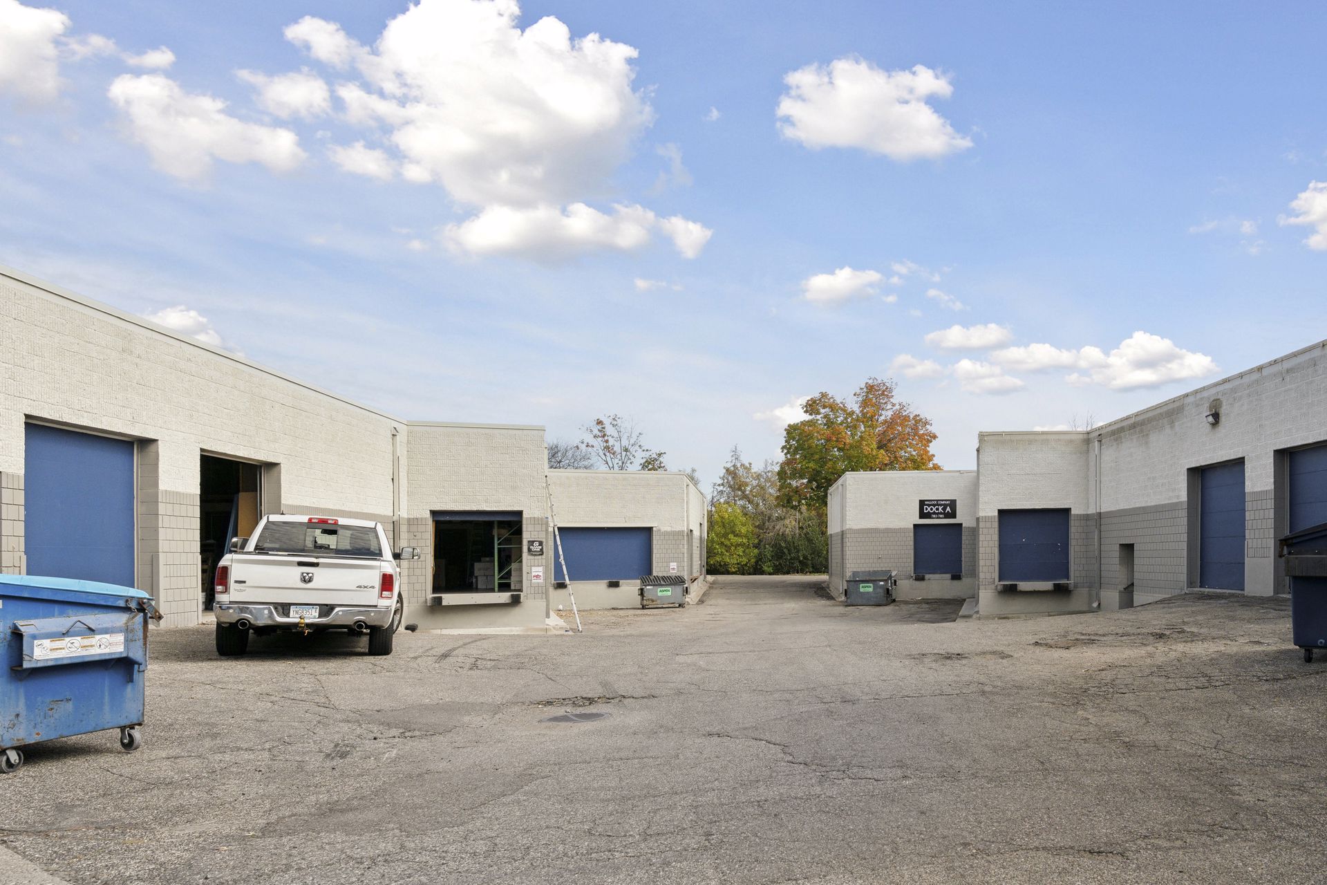 Rear service courtyard between two building wings with blue overhead doors and a waste container