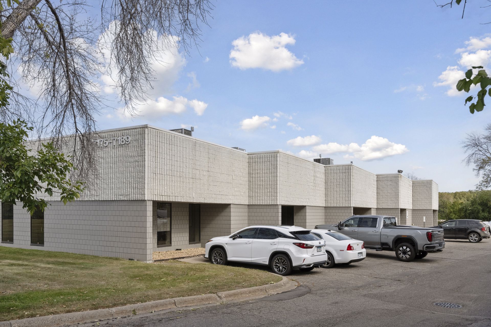 Corner of a light grey block building with projecting bays and cars parked along the front