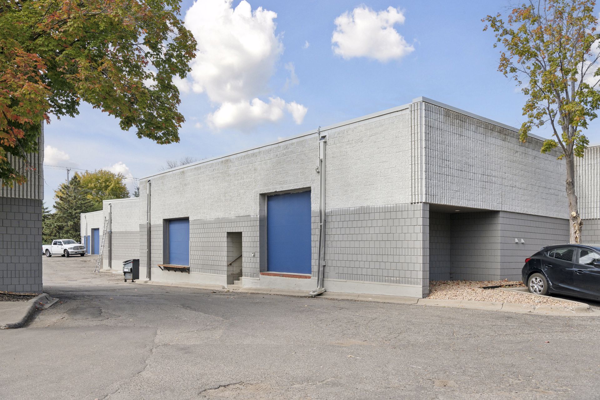 Rear elevation of a grey block building with two blue overhead loading doors and a pedestrian door