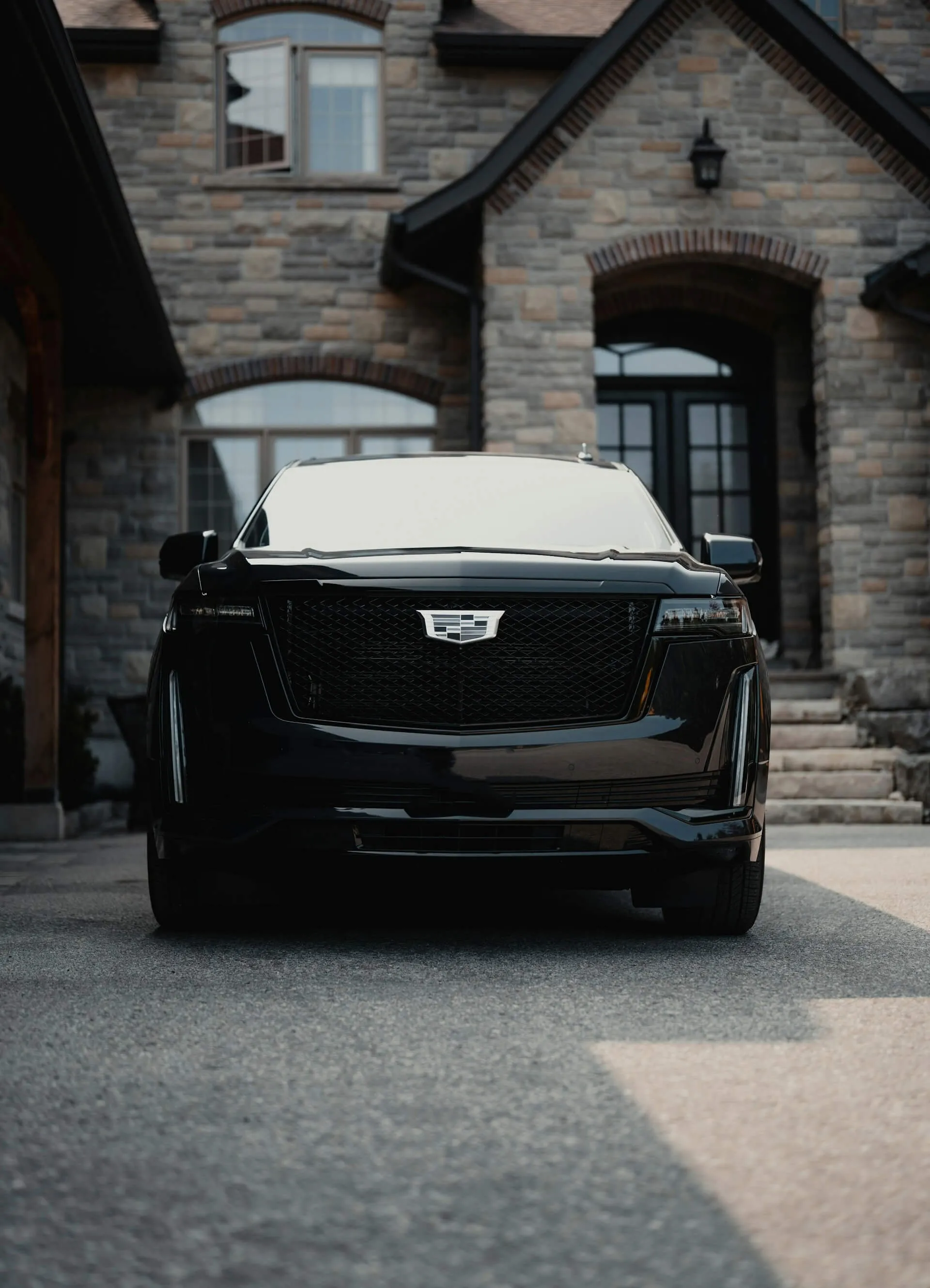 Black Cadillac SUV parked in the driveway of a stone house