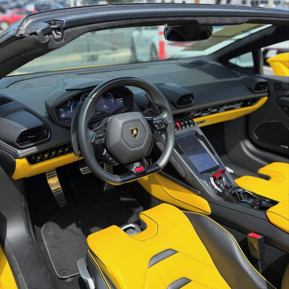 Interior of a Lamborghini car showing black steering wheel and yellow sporty seats and dashboard.