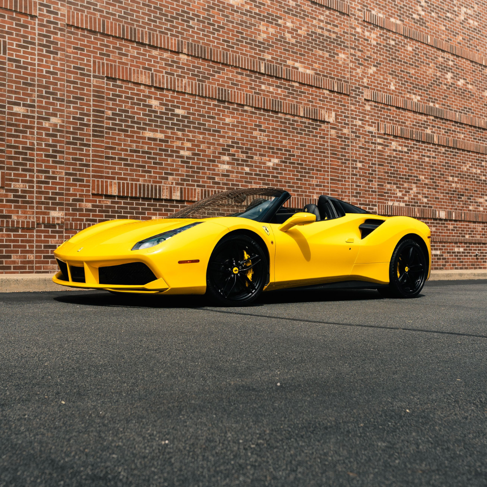 Yellow Ferrari convertible sports car parked in front of a red brick wall.