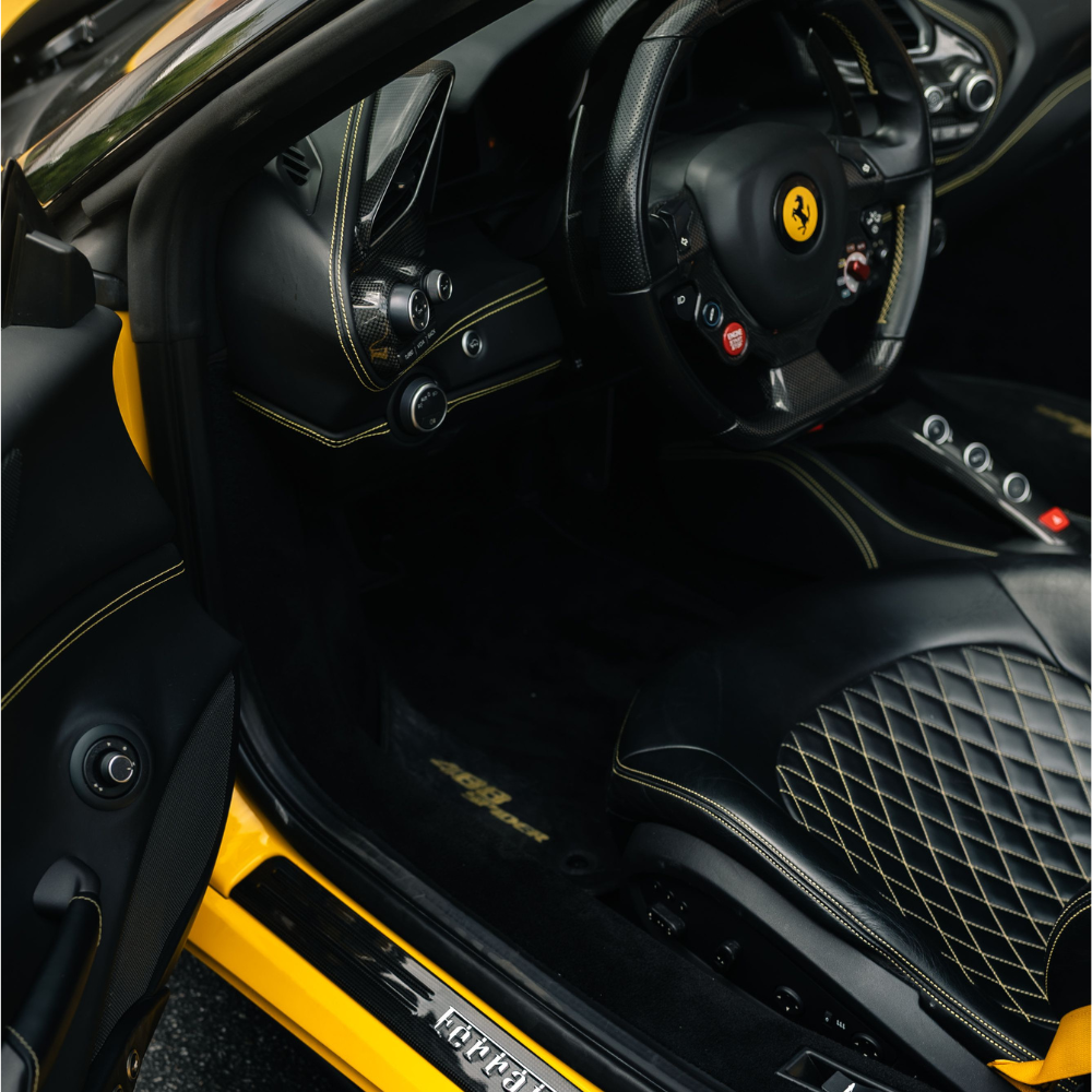 Interior of a yellow Ferrari showing black quilted leather seat and steering wheel with logo.