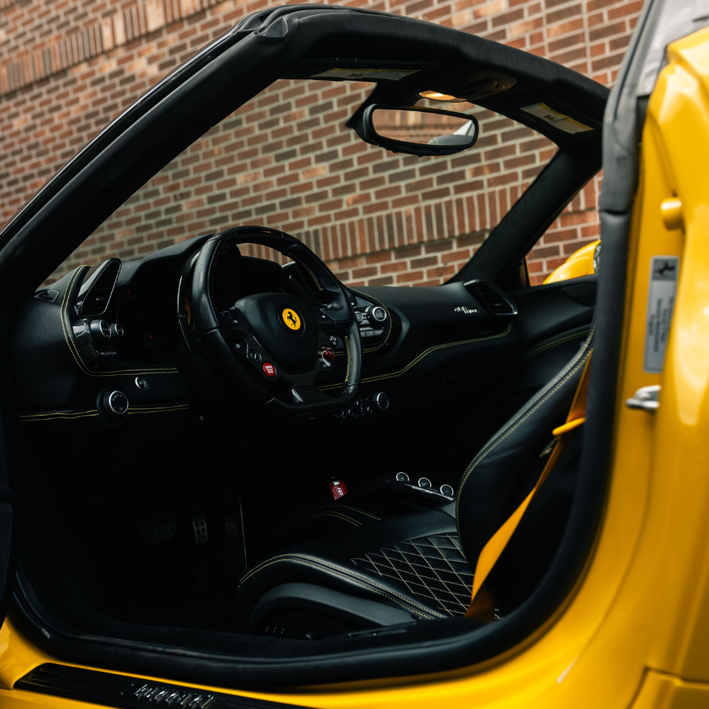 Interior of a yellow Ferrari sports car with black leather seats and detailed steering wheel.