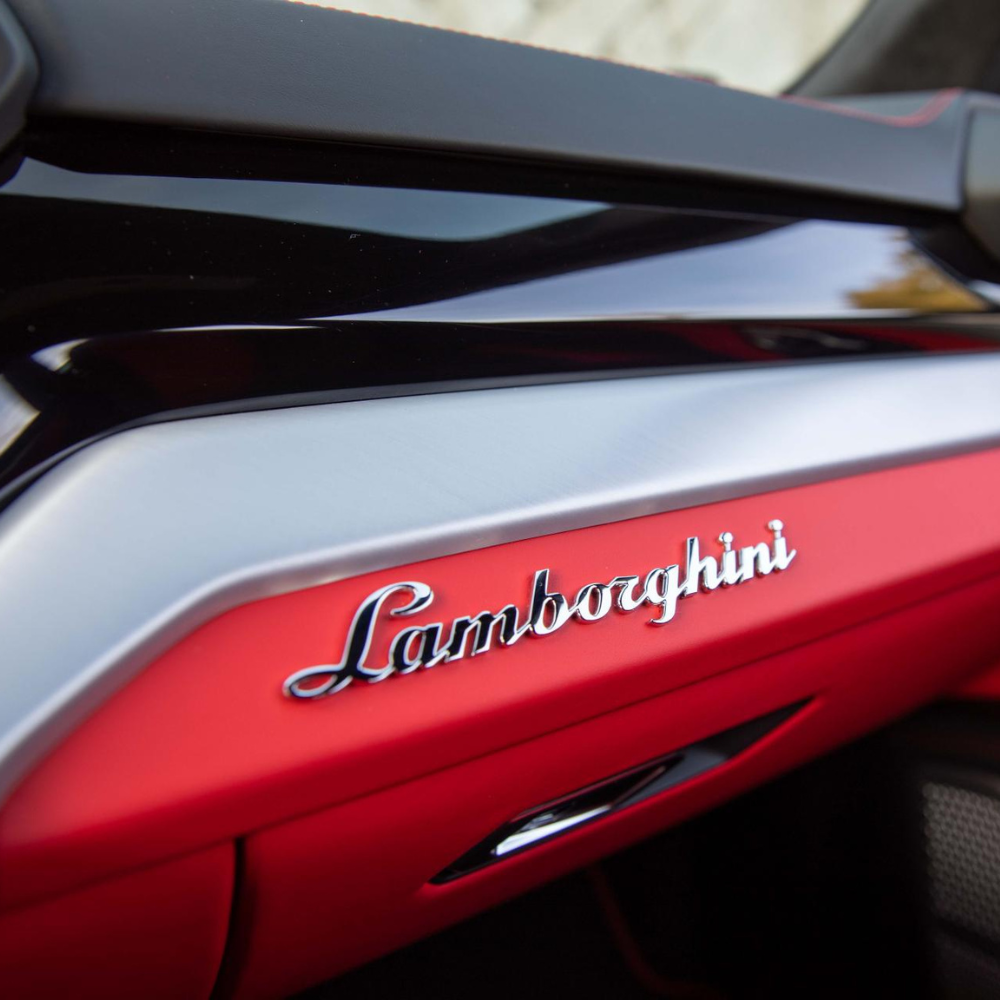 Close-up of Lamborghini logo on a car interior with red and black trim.