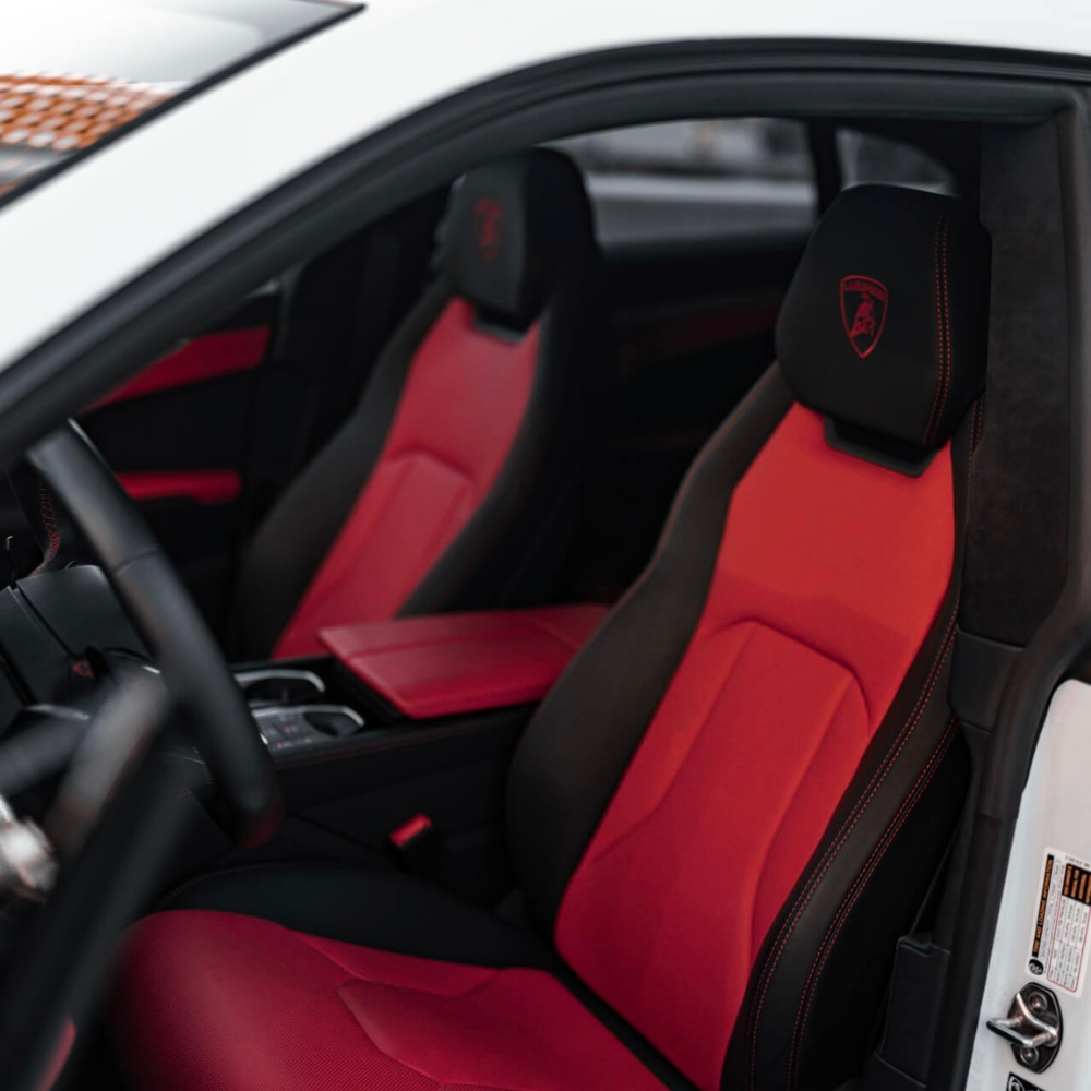 Interior of a car showing black and red leather seats with a Lamborghini logo on the headrests.