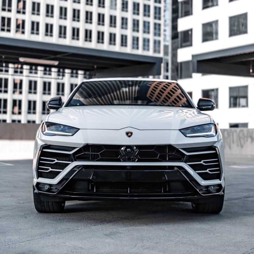 Front view of a white Lamborghini Urus parked outdoors with building reflections on its hood.