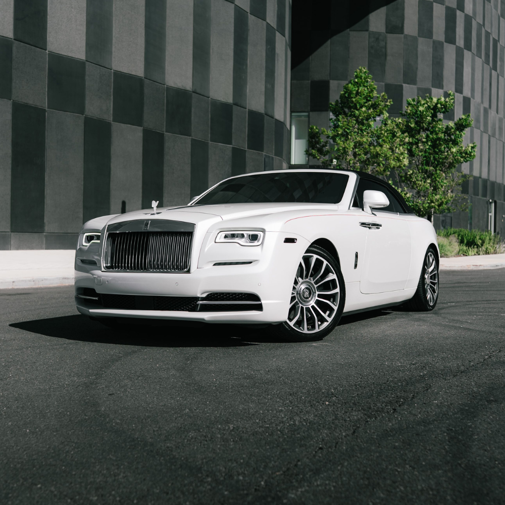 White Rolls-Royce convertible parked on street in front of a modern building with checkered facade.