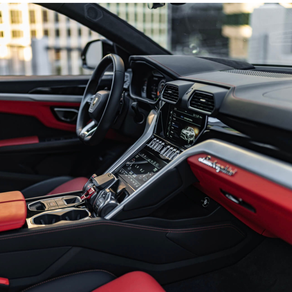 Interior of a Lamborghini car showing the steering wheel, dashboard, touchscreen, and red and black leather seats.