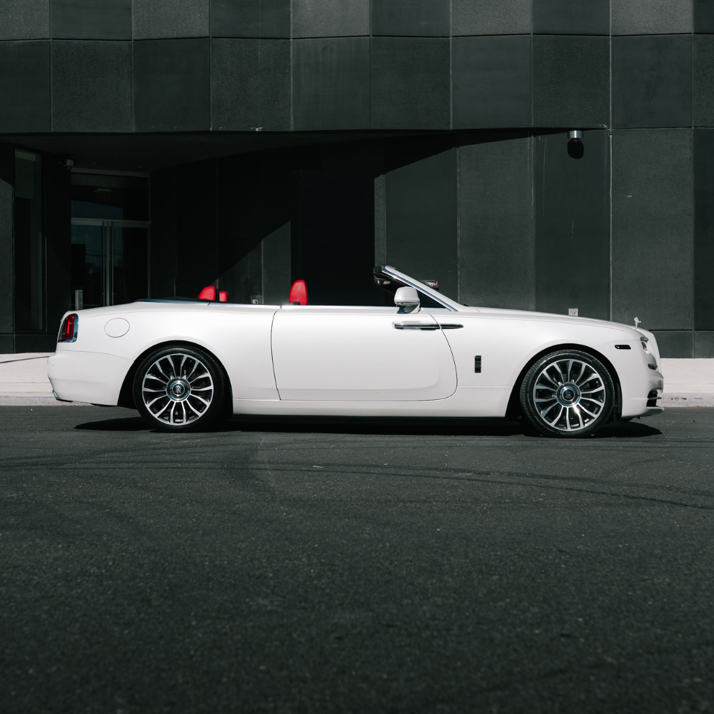 White convertible luxury car with red interior parked beside a black modern building.
