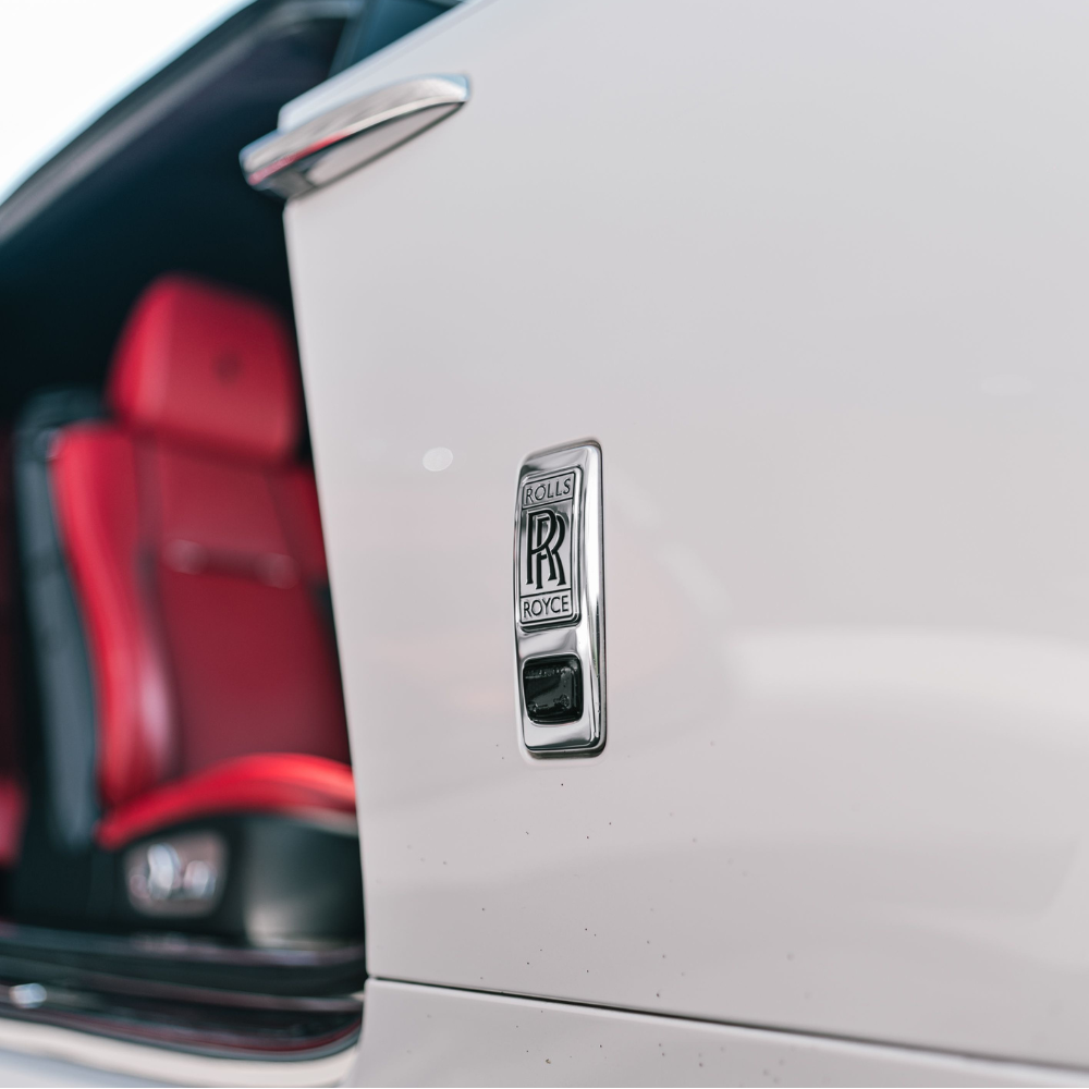 Close-up of a white car door with Rolls-Royce emblem and red leather interior seats.