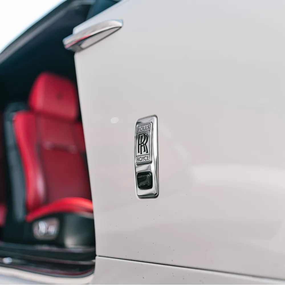 Close-up of the Rolls-Royce badge on a white Dawn with red seats behind