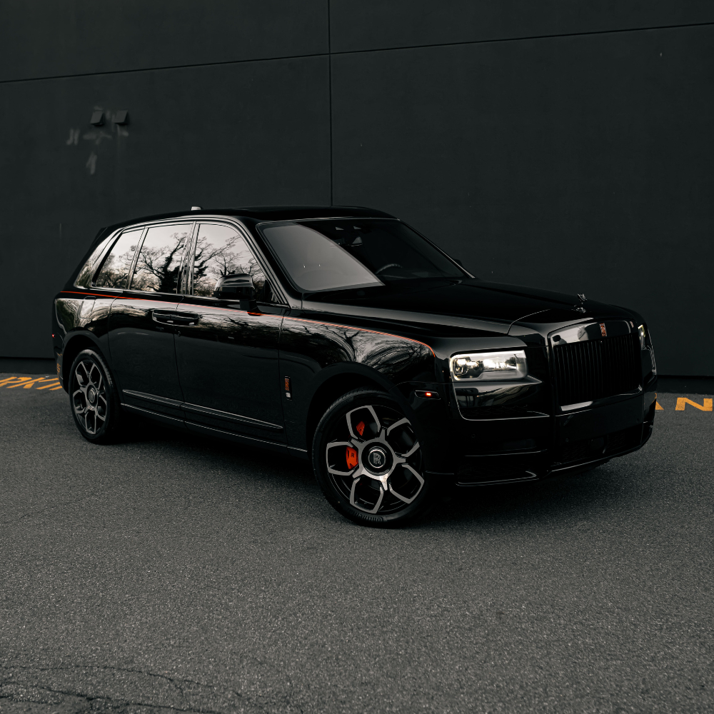 Black luxury Rolls-Royce Cullinan SUV parked in front of a dark wall with reflections on its windows.