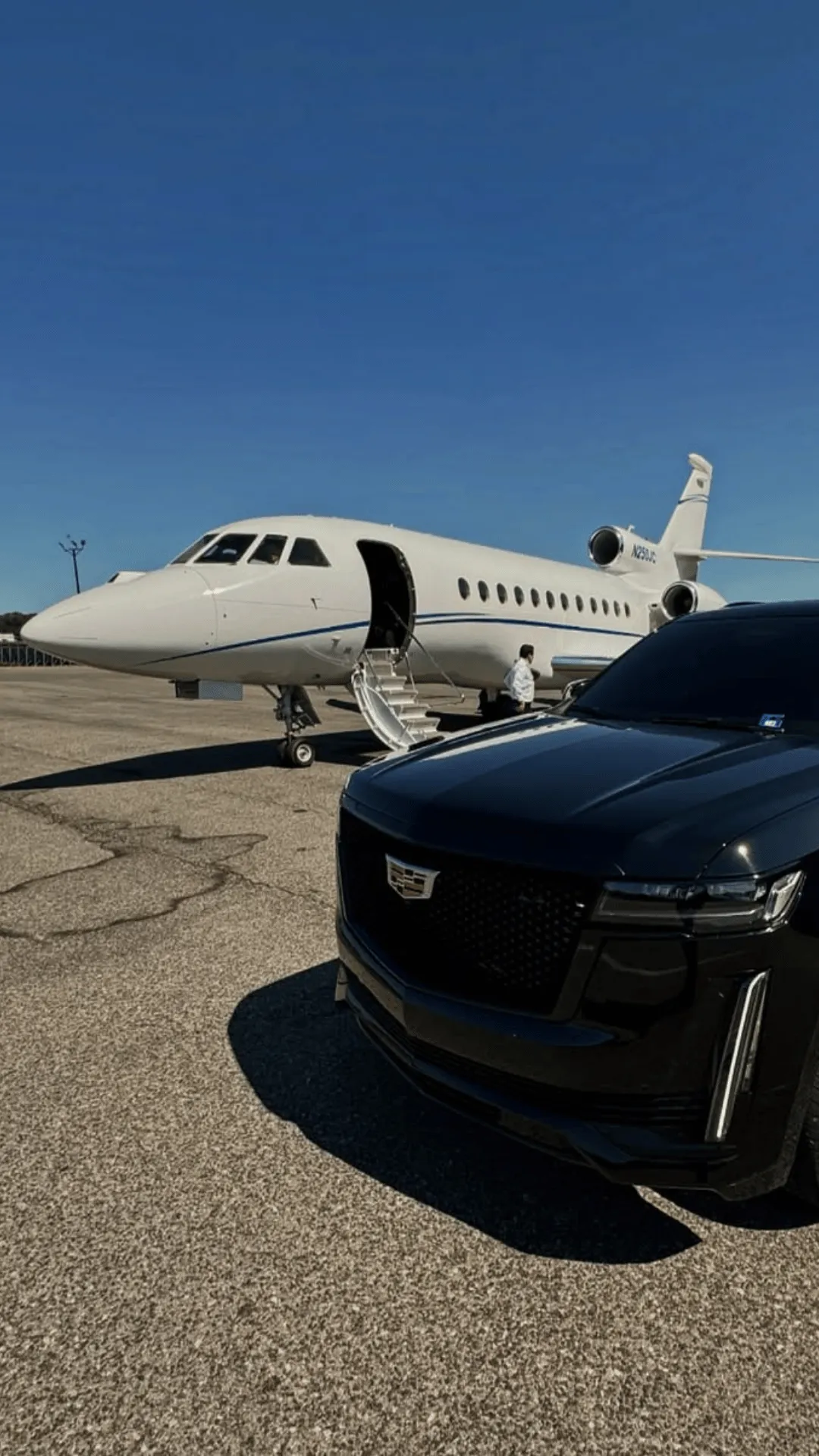 Black Cadillac SUV parked on an airport tarmac beside a white private jet