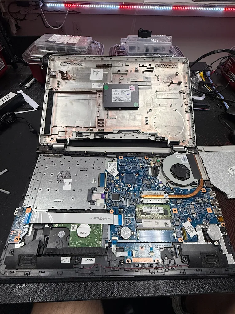 Open laptop showing its motherboard, storage drive, cooling fan, and internal components during repair