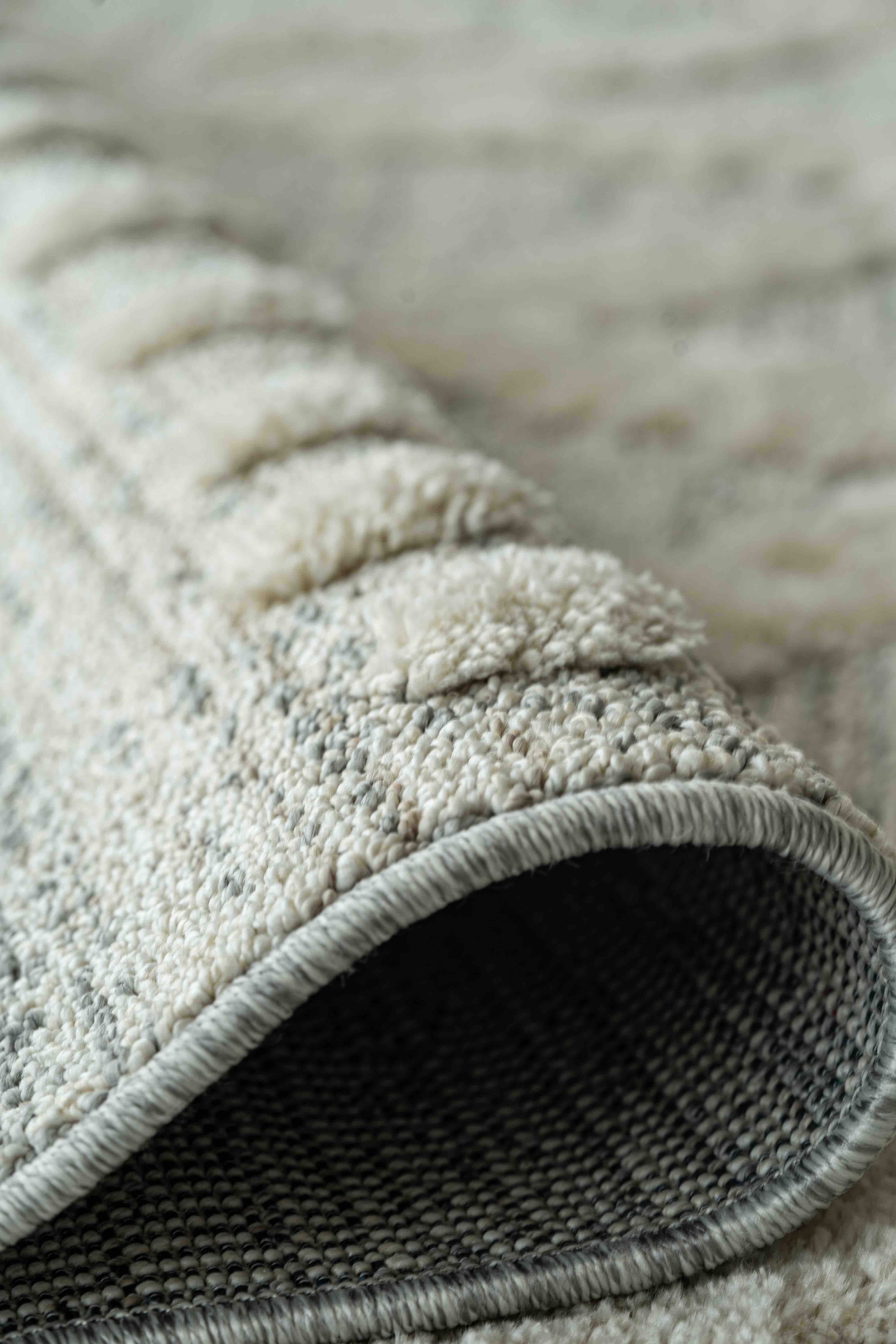 Close-up of a rolled-up textured beige and gray rug showing its woven underside and soft looped pile surface.