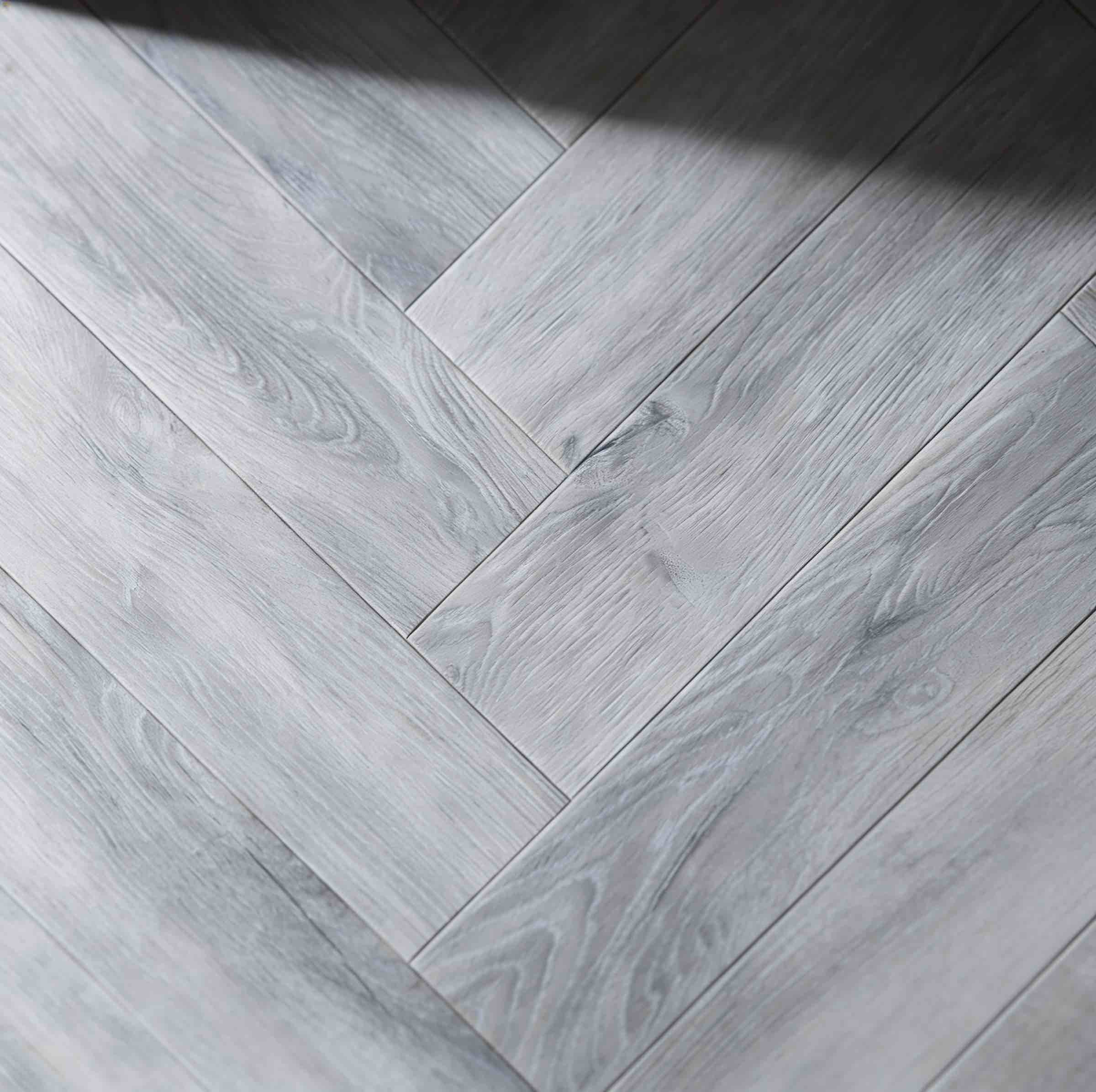 Close-up of light gray wooden floor with a herringbone pattern showing wood grain texture.