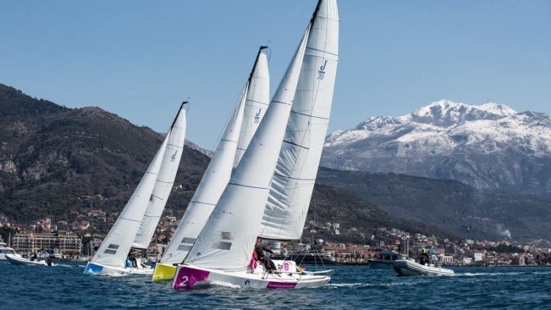 Sailing yachts racing with snow-capped mountains in the background.