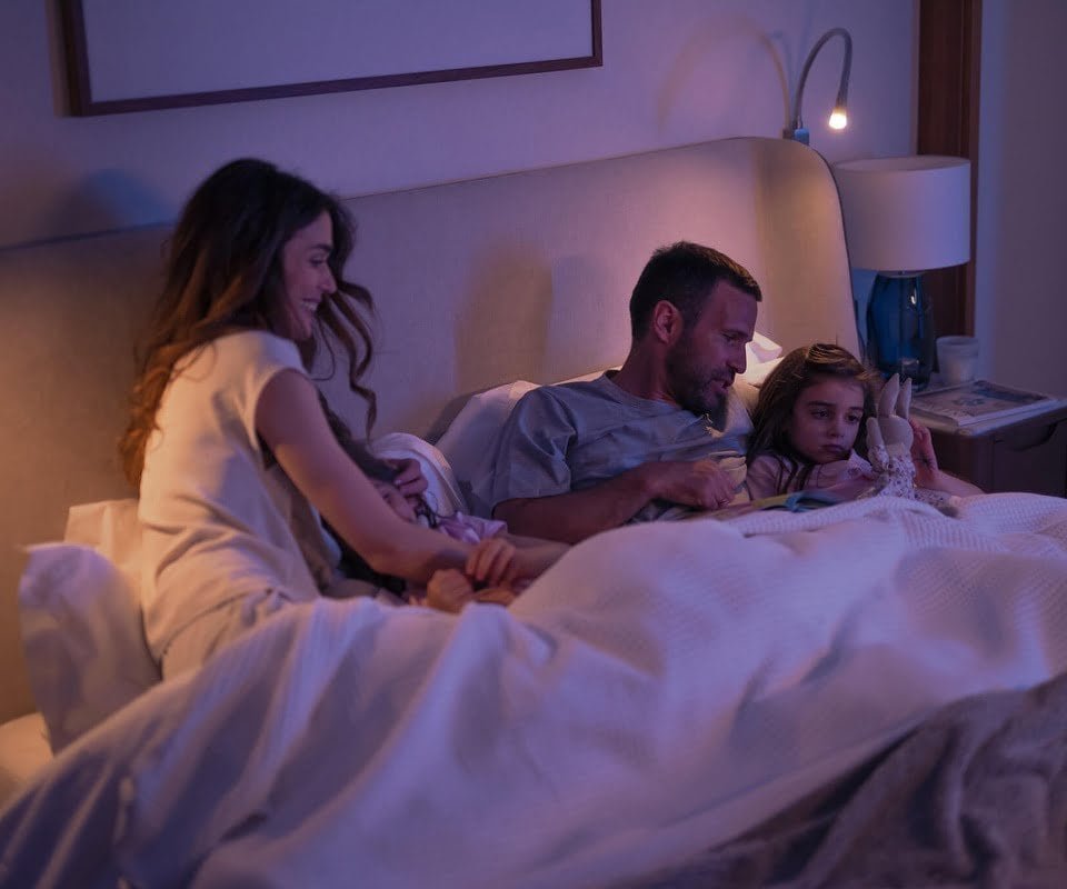 Family enjoying bedtime together in a cozy, warmly lit bedroom setting.