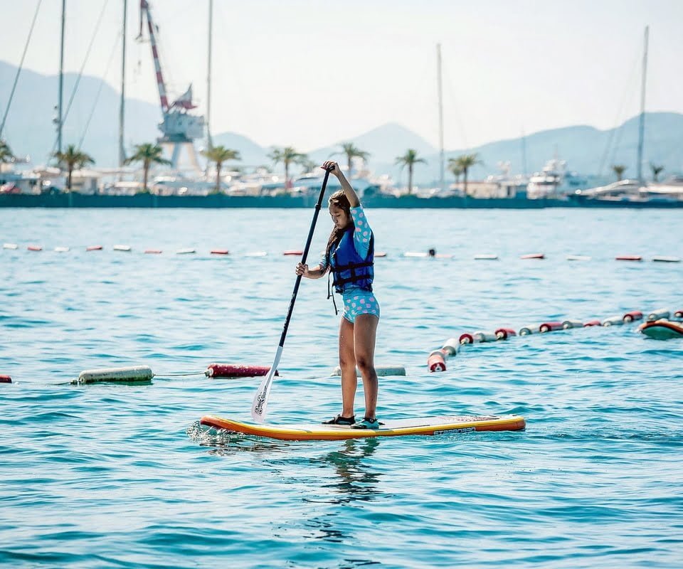 Paddleboarding on calm waters with scenic marina views and mountain backdrop.