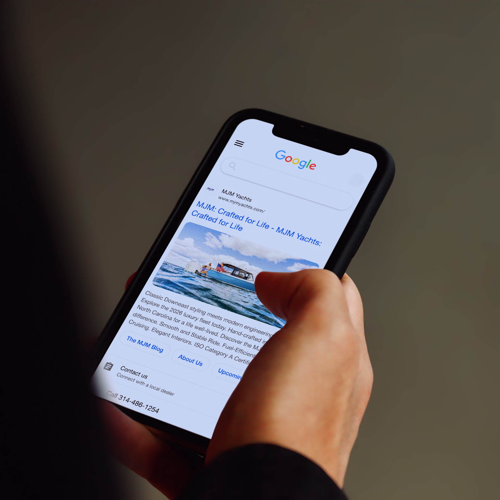 A hand holding a phone looking at a google search ad for MJM yachts