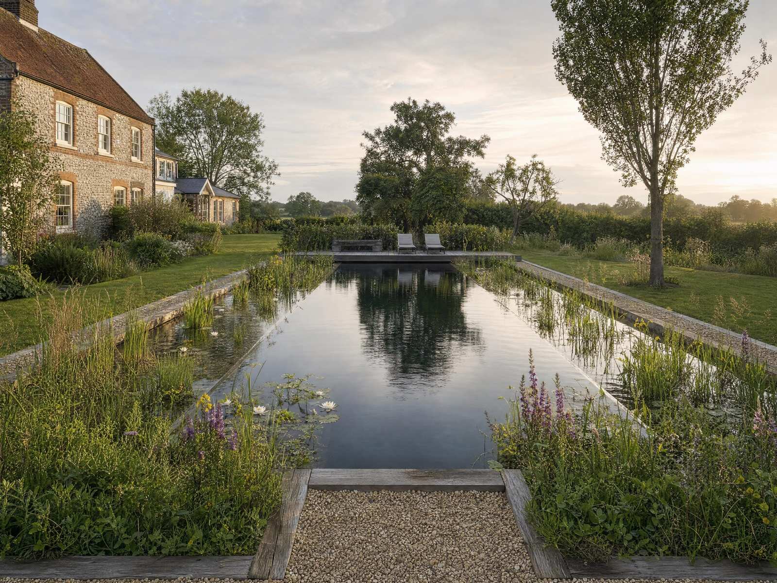 Natural swimming pond with planted margins and flowering perennials beside a country house