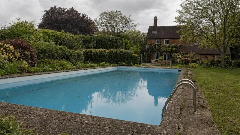 A gravel path and ornamental grasses running past a pool towards a red brick manor house