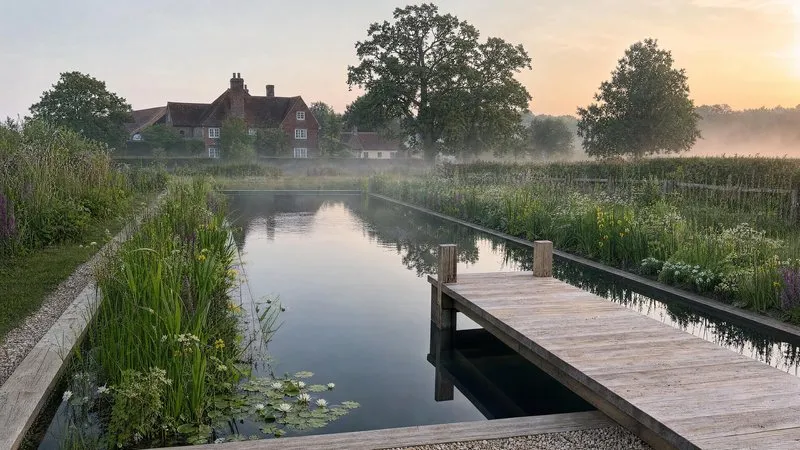 A planted natural pond with a gravel path running towards a manor house