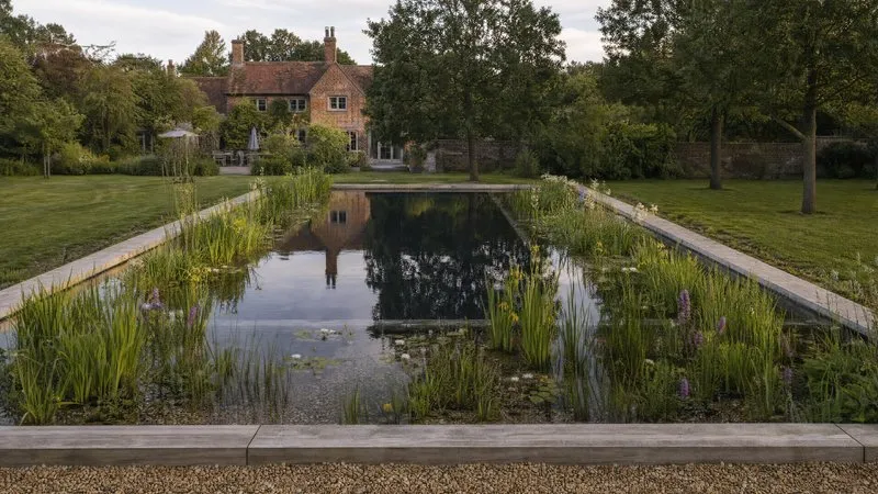 A pond reflecting a manor house, with timber decking and established planted margins