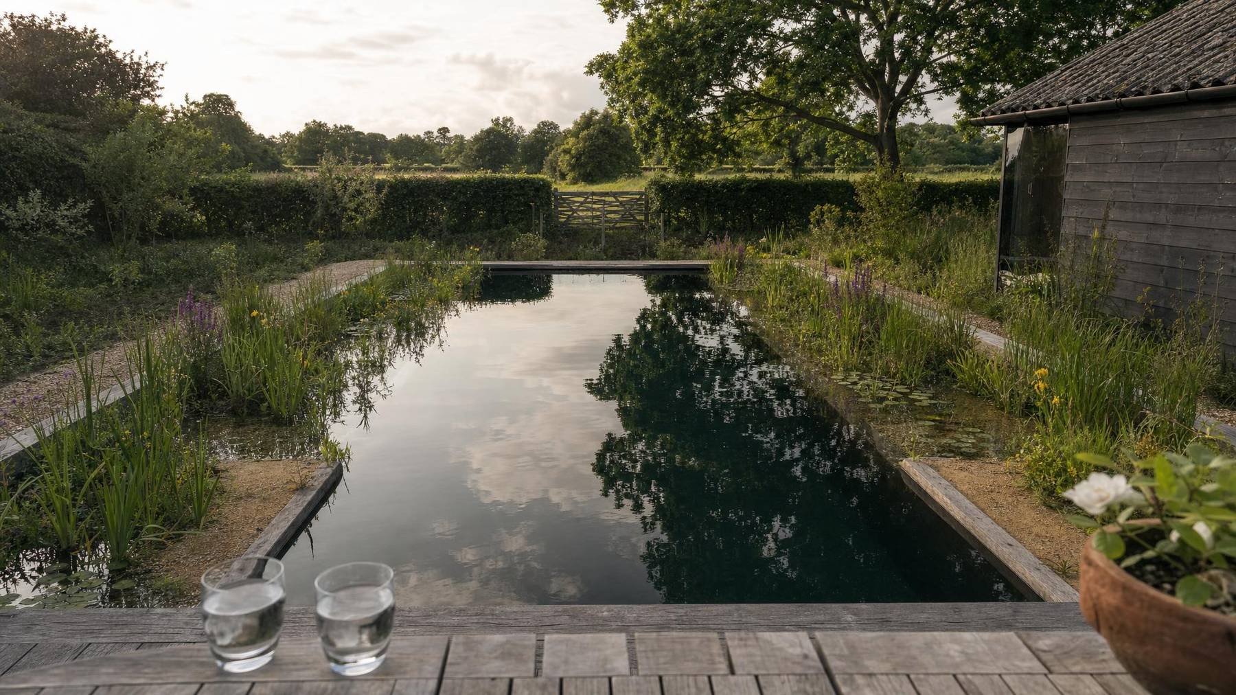 A planted natural pond with a gravel path curving towards a manor house