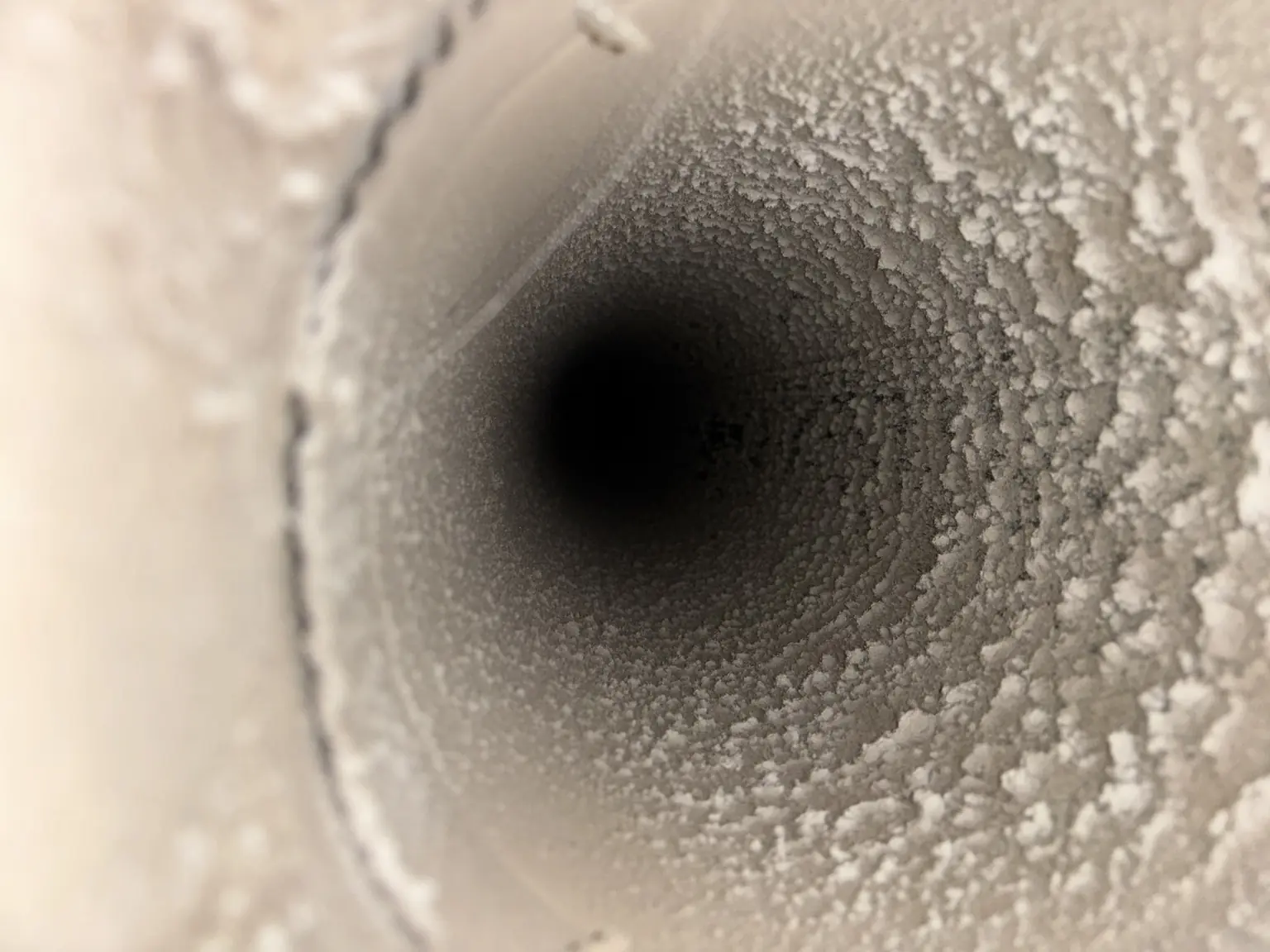 Close-up inside a round air duct coated with thick dust buildup before cleaning.