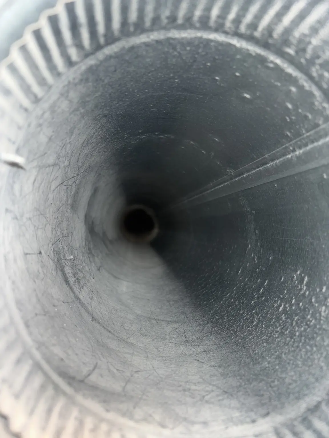 Inside view of a round metal air duct showing some dust and debris build-up.