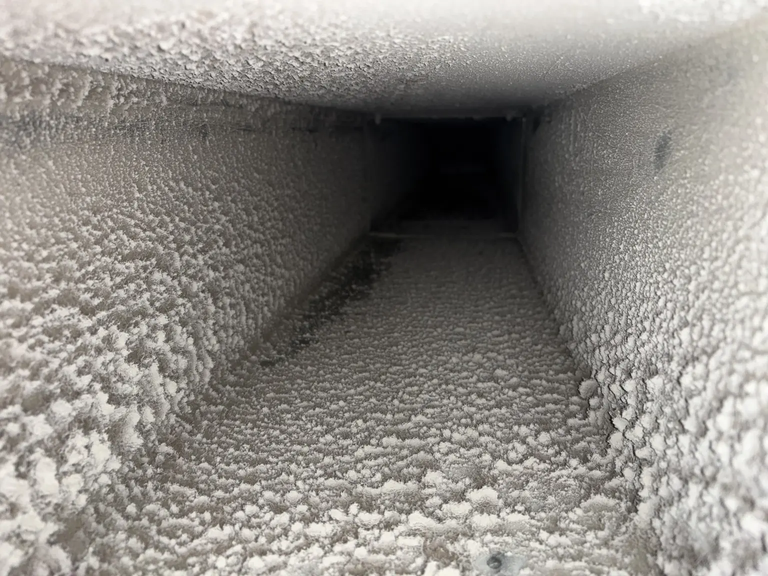 Close-up inside view of an air duct heavily coated with dust and dirt buildup.