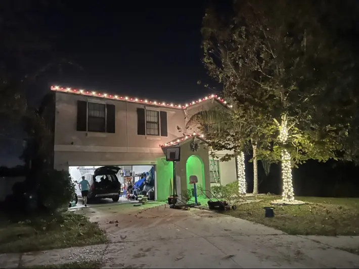 Home decorated with red and white roofline lights and wrapped trees