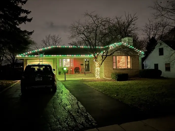 Home decorated with green and white roofline lights and a lit tree
