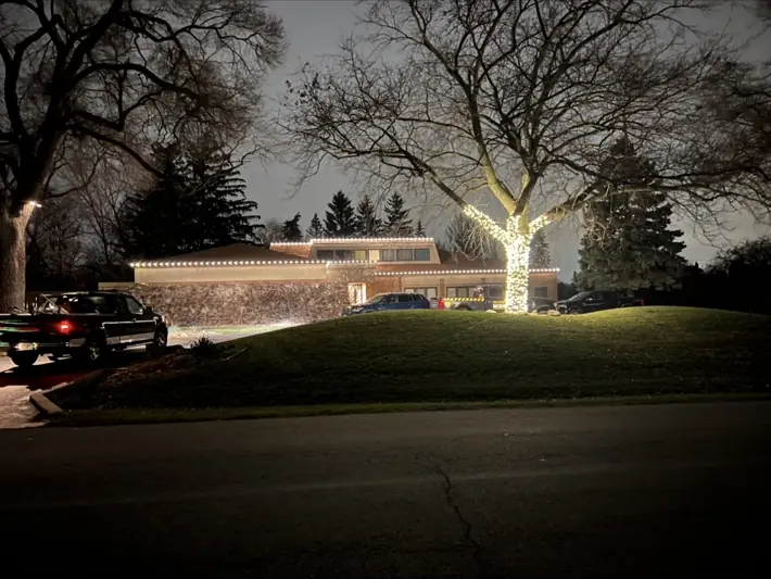 Home with warm white roofline lights and wrapped tree lighting