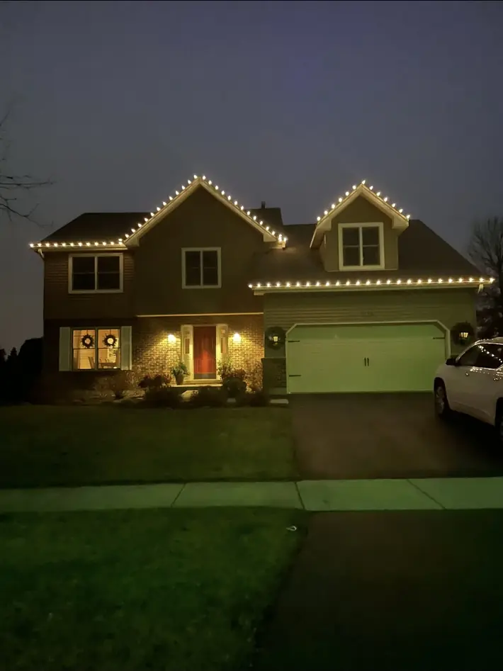 Home with warm white holiday lights outlining multiple roof gables