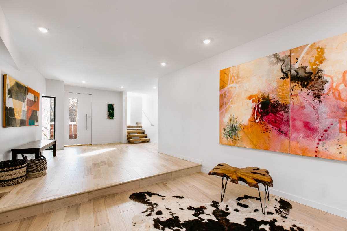 Bright contemporary entryway with light wood floors, white walls, a large colorful abstract painting, a cat-legged wooden side table, two woven baskets, and a black and white cowhide rug.