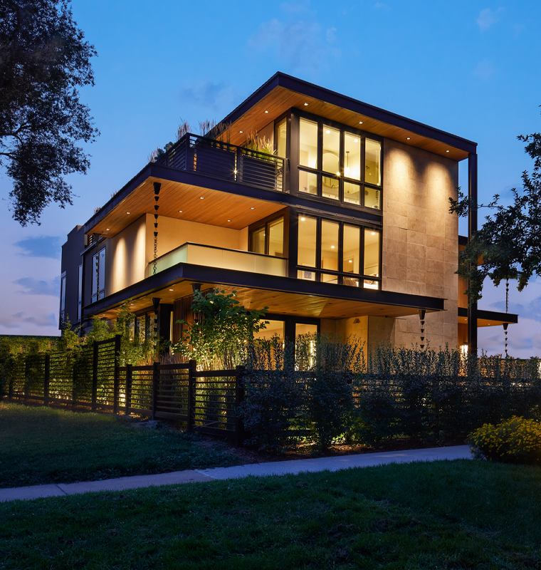 Three-story modern home lit at dusk, viewed from the corner