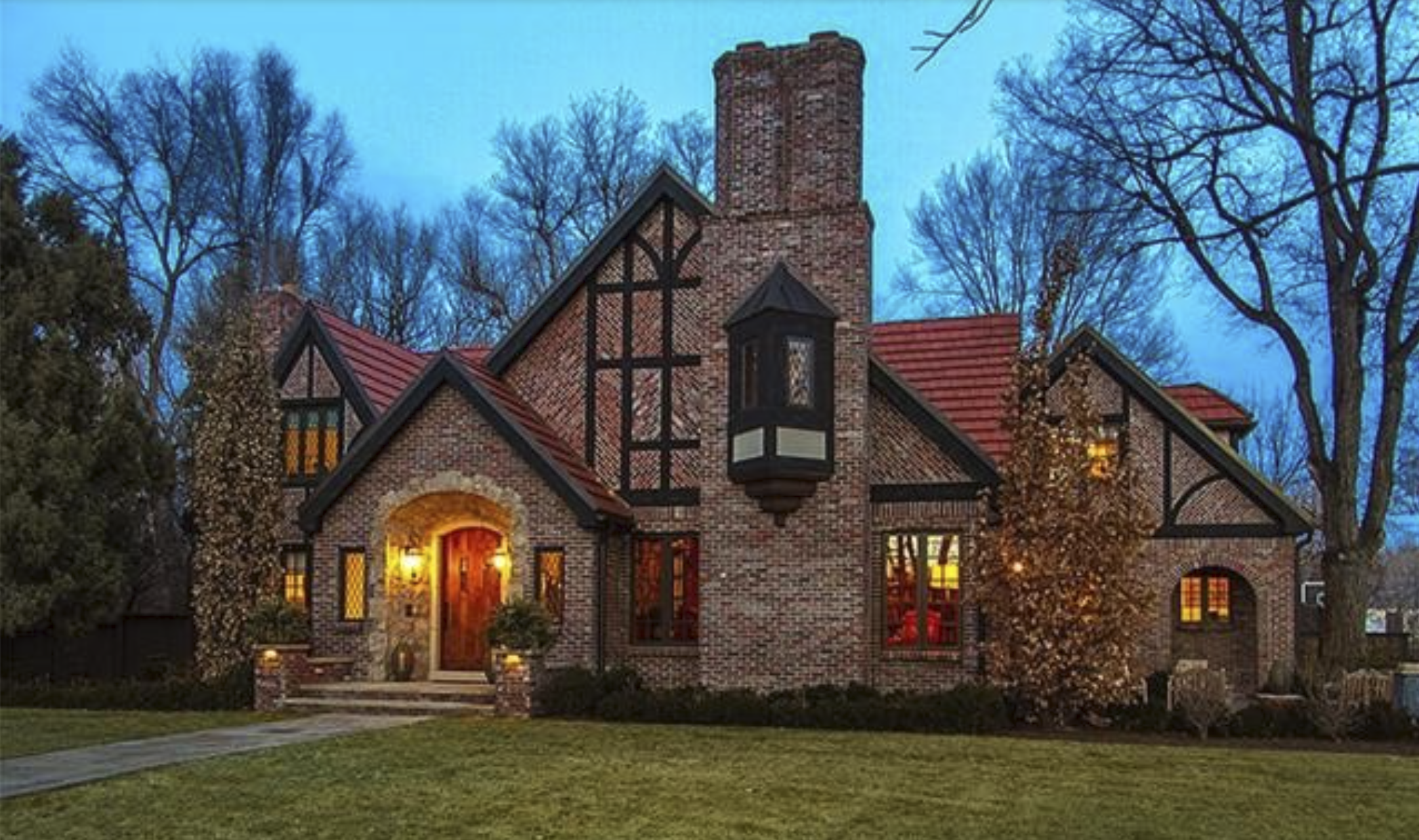 Tudor-style brick custom home with half-timbered gables and a tall chimney at dusk in Englewood