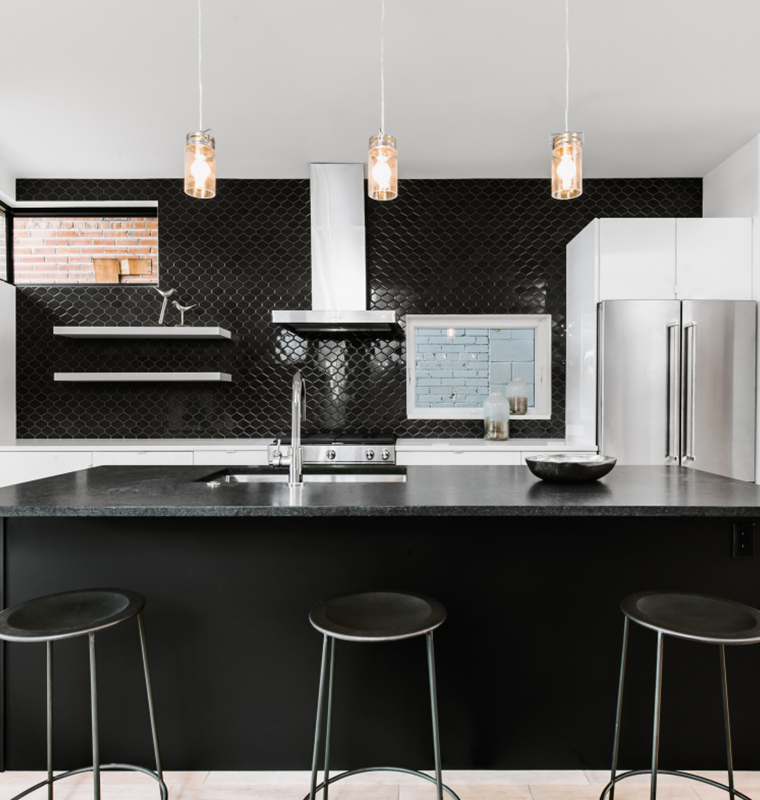 Modern kitchen with black island, black tile backsplash and glass pendant lights