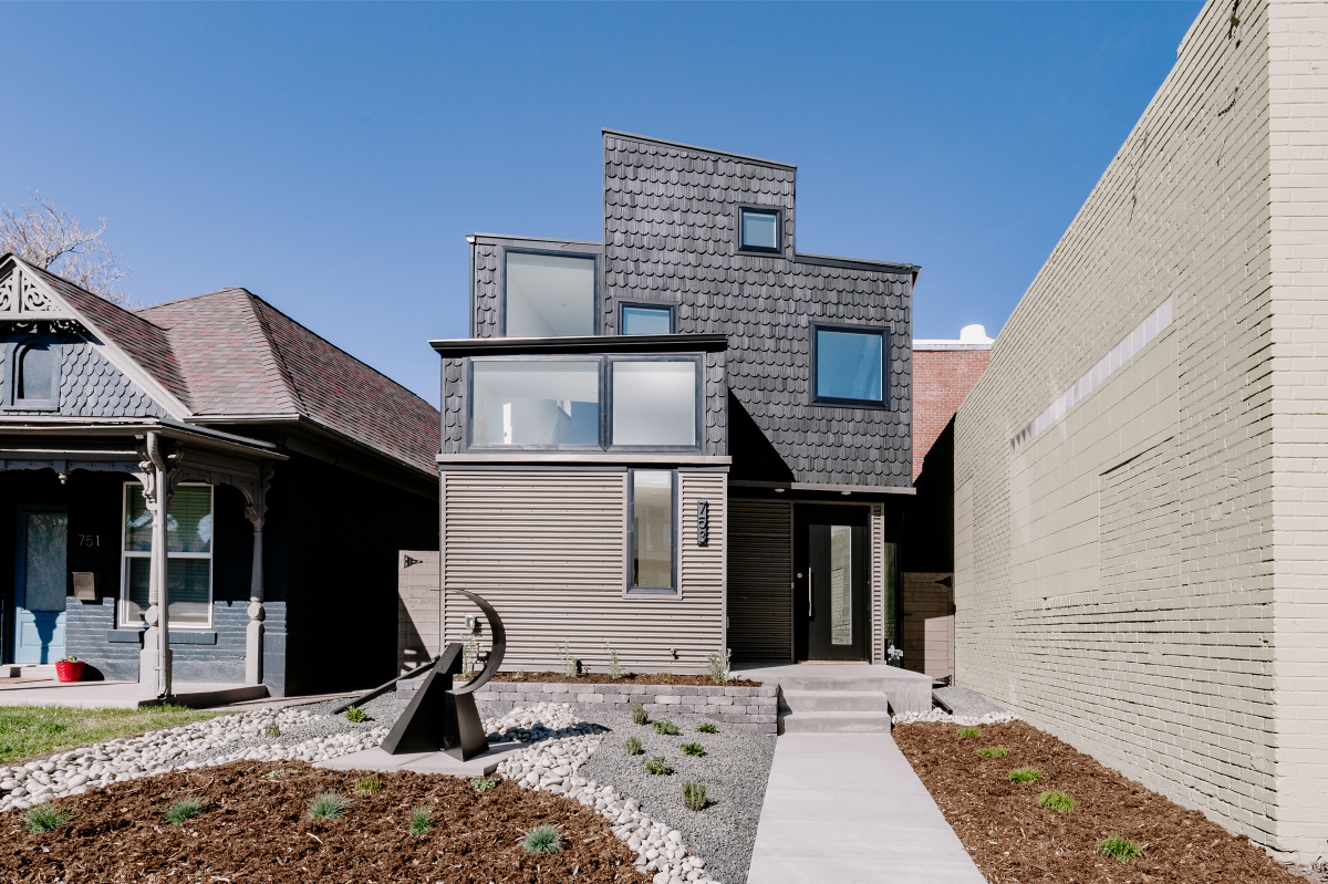 Modern infill home with dark shingle and corrugated metal siding next to a Victorian house